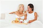 Woman giving a piece of croissant to her fiance in their bedroom