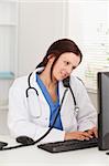 A female doctor is sitting in an office and telephones whilst typing