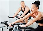 Young athletic couple spinning veloargometers in gym, female on focus