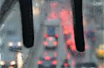 Raindrops macro on glass overpass surface and blurry city traffic lights.