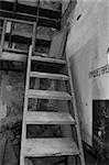 Wooden crumbling attic staircase and fire extinguisher sign in abandoned factory interior. Black and white.