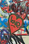 Dirty love graffiti over messy tagged urban wall background. Heart of the city.