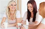 Laughing young Women sitting at a table with cups in a kitchen