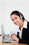 A smiling young operator with a headset is helping someone via headset in her office