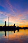 The silhouette of an oil refinery at sunset, against a radient sky