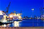 Image of a city port with intense blue saturated color. Boats are on the water, and the city of Rotterdam is viewable in the background. No people. Horizontally framed shot.