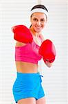 Smiling pretty fitness girl in boxing gloves punching