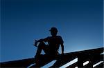 Builder or carpenter resting on top of roof structure - silhouette with strong back light