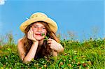 Young teenage girl laying in summer meadow resting chin on hand smelling flower