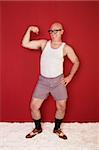 Funny bald muscular man shows off his biceps over maroon background