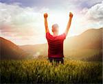 Young man with arms raised looking at sunset with mountains ahead