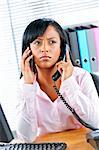 Young black business woman multitasking using two phones in office