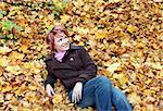 Young pretty woman lies in yellow leaves in park