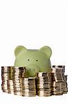 Green piggy bank surrounded by stacks of golden coins on a white background.