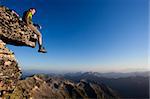 Young man sitting on rock above mountain range