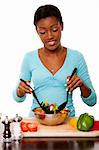 Beautiful health conscious young woman tossing healthy organic salad in kitchen, isolated.