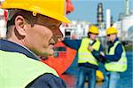 Portrait of a docker in front of a harbor scene with two of his coworkers out of focus in the background