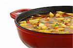 Closeup of big red saucepan with fresh hot ragout with meat, potatoes and vegetables isolated on white background