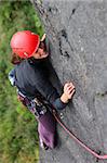 Smiling woman with helmet climbing basalt rock