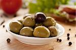 Green olives in a bowl on  a wooden board.