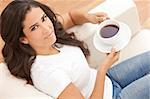 A beautiful young Latina Hispanic woman or girl with a wonderful enigmatic smile drinking tea or coffee from a white cup at home on her sofa