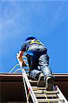 Construction worker climbing extension ladder to roof