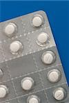 Close-up of a pack of white pills on blue background.