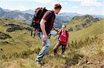 A young male hiker is helping a female hiker to climb a mountain in the Alps.