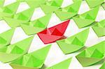 One red and several green paper boats on white background