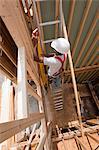 Hispanic carpenter carrying a level up ladder to second floor at a house under construction