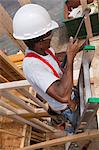 Hispanic carpenter using a hammer on a ladder at a house under construction