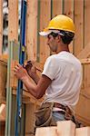 Charpentier hispanique marquant une mesure sur une planche dans une maison en construction