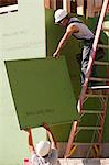 Charpentiers hispaniques en tirant le revêtement extérieur vers le haut de l'échelle dans une maison en construction