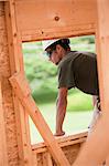 Hispanic carpenter looking out from the window opening of second floor at a house under construction