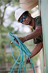 Carpenter passing coiled air hose through the window of a house under construction