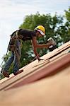 Hispanic carpenter using a nail gun on the roofing of a house under construction