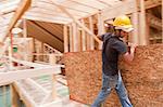 Hispanic carpenter carrying sheathing at a house under construction