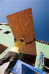 Hispanic carpenters carrying sheathing at a house under construction
