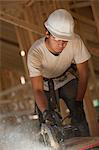 Carpenter using a circular saw on roof panel at a house under construction