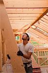 Hispanic carpenter passing up a rafter to roof at a house under construction