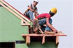 Hispanic carpenters at roof edge measuring to trim