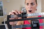 Woman weighing herself on a weighing scale and looking shocked