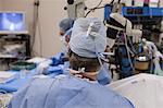 Doctor looking in microscope during surgery with surgical technician taking next instrument