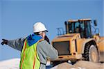 Engineer talking on a walkie-talkie directing front end loader at a construction site