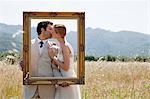 Newlyweds holding vintage picture frame, kissing