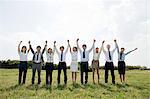 Businesspeople in a row in field, arms up