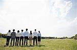 Businesspeople in a row in field, rear view