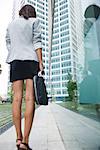 Woman standing on sidewalk with briefcase, low angle view