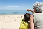 Grandmother and grandson sitting together on beach, looking at sea