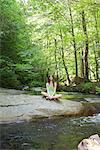 Young woman sitting on rock beside stream